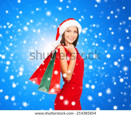 sale, gifts, christmas, holidays and people concept - smiling woman in red dress with shopping bags over blue snowy background
