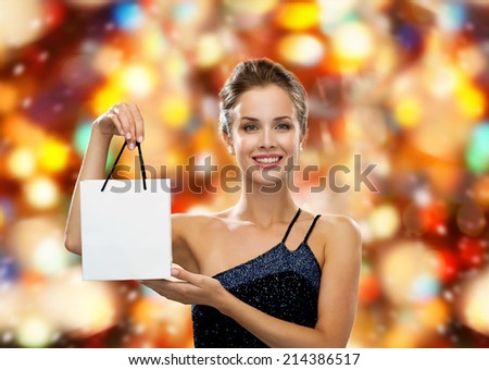 luxury, advertisement, winter holidays, christmas and sale concept - smiling woman with white blank shopping bag over red lights background