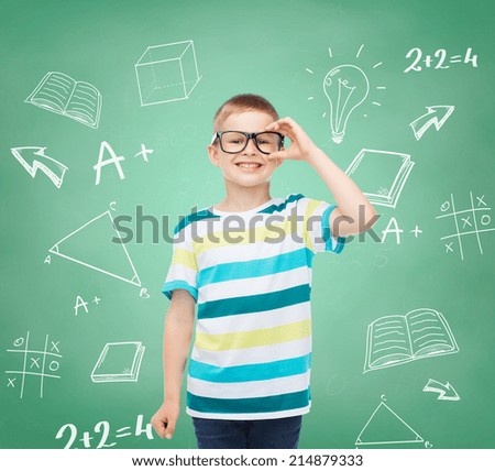 vision, education, childhood and school concept - smiling little boy in eyeglasses over green board with doodles background