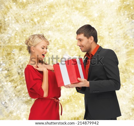 christmas, holidays, valentine\'s day, celebration and people concept - smiling man and woman with present over yellow lights background