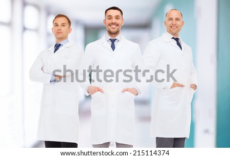 healthcare, profession, teamwork and medicine concept - smiling male doctors in white coats over hospital corridor background