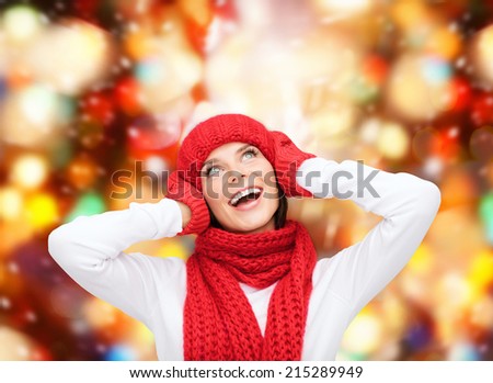happiness, winter holidays, christmas and people concept - smiling young woman in red hat, scarf and mittens over lights background