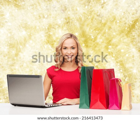 christmas, holidays, technology, advertising and people concept - smiling woman in red blank shirt with shopping bags and laptop computer over yellow lights background