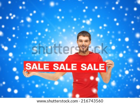 sale, shopping, christmas, holidays and people concept - smiling man in red t-shirt with sale sign over blue snowy background