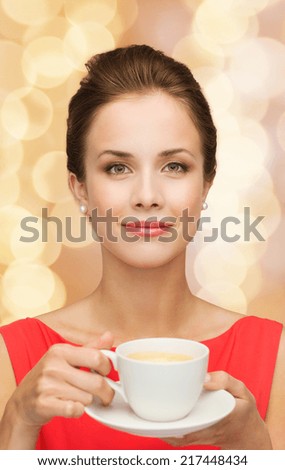 leisure, happiness and drink concept - smiling woman in red dress with cup of coffee over golden lights background