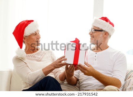 family, holidays, christmas, age and people concept - happy senior couple in santa helper hats with gift box at home