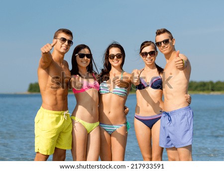 friendship, sea, holidays, gesture and people concept - group of smiling friends wearing swimwear and sunglasses showing thumbs up on beach