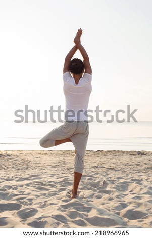 fitness, sport, people and lifestyle concept - man making yoga exercises on sand outdoors from back