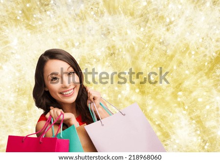 happiness, winter holidays, christmas and people concept - smiling young woman with shopping bags over yellow lights background