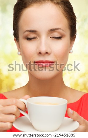 leisure, happiness and drink concept - smiling woman in red dress with closed eyes holding cup of coffee over golden lights background