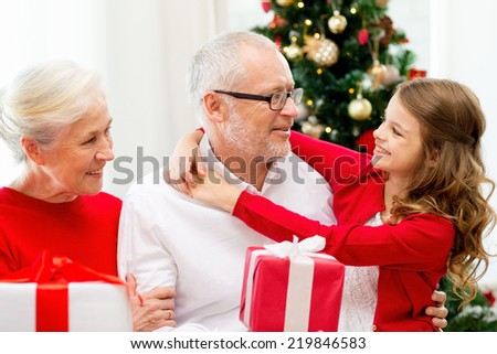 family, holidays, generation, christmas and people concept - smiling grandparents and granddaughter with gift boxes sitting on couch at home