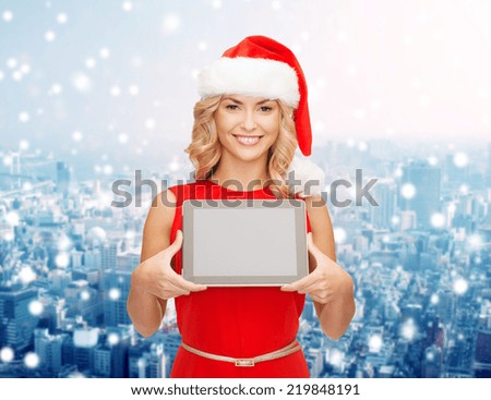 christmas, technology, present and people concept - smiling woman in santa helper hat with tablet pc computer showing blank screen over snowy city background