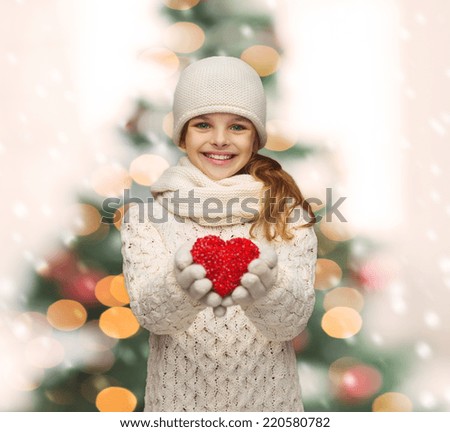 holidays, happiness, charity concept - smiling teenage girl in winter clothes with small red heart