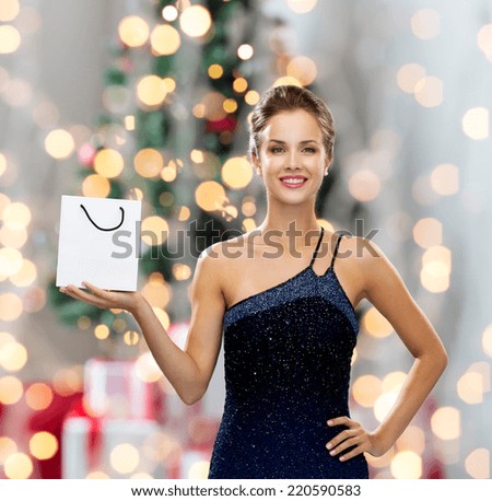 sale, advertisement, holydays and people concept - smiling woman with white blank shopping bag over christmas tree and lights background