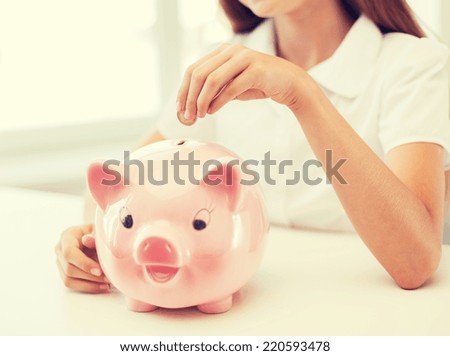 education, school and money saving concept - smiling child putting coin into big piggy bank