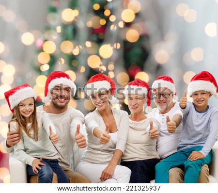 family, generation, gesture, holidays and people concept - happy family in santa helper hats showing thumbs up over christmas tree lights background