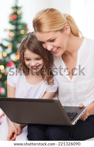 family, childhood, holidays, technology and people - smiling mother and little girl with laptop computer over living room and christmas tree background