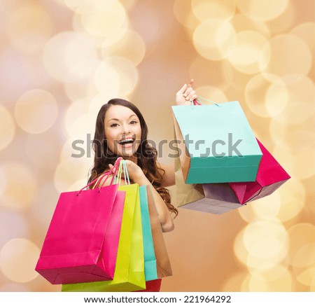 sale, gifts, holidays and people concept - smiling woman with colorful shopping bags over beige lights background