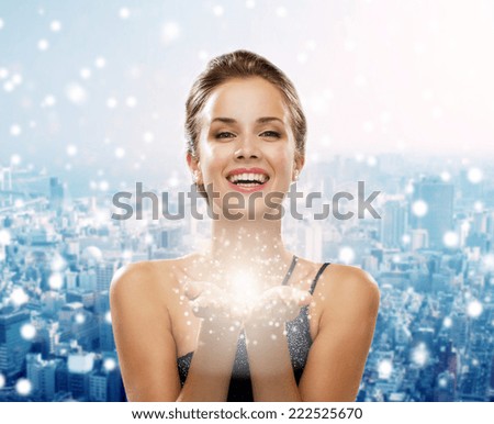 people, holidays, christmas and magic concept - laughing woman in evening dress holding something over snowy city background