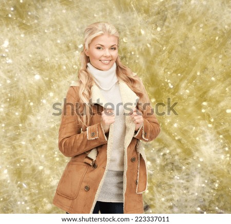 winter holidays, christmas, fashion and people concept - smiling young woman in winter clothes over yellow lights background