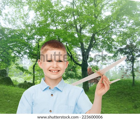 dreams, future, hobby, nature and childhood concept - smiling little boy holding wooden airplane model in his hand over park background