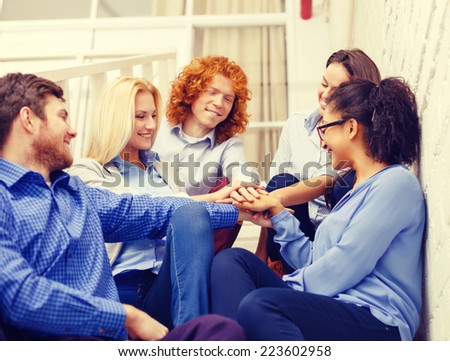 business, office, gesture and startup concept - smiling creative team with hands on top of each other sitting on staircase