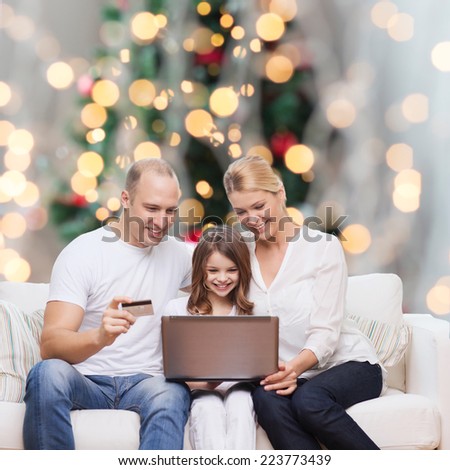 family, holidays, shopping, technology and people concept - happy family with laptop computer and credit card over christmas lights tree background