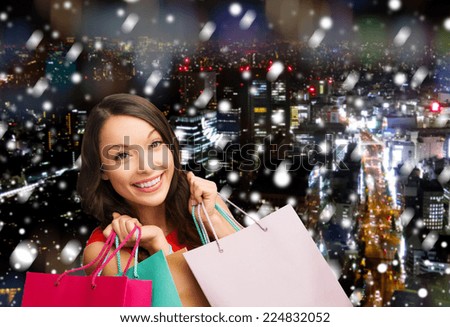 happiness, winter holidays, christmas and people concept - smiling young woman with shopping bags over snowy night city background