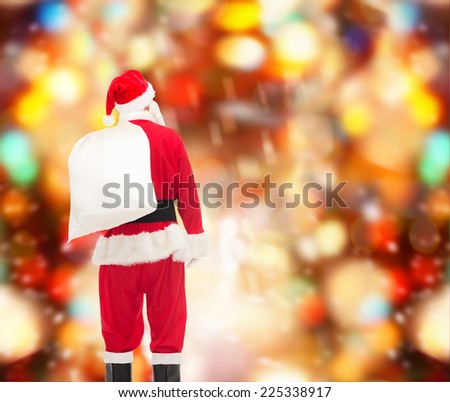christmas, holidays and people concept - man in costume of santa claus with bag from back over red lights background