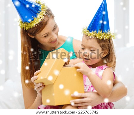 family, childhood, holidays and people concept - happy mother and daughter in blue party hats with gift box
