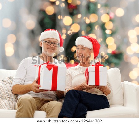 family, holidays, christmas, age and people concept - happy senior couple in santa helper hats with gift boxes over tree lights background