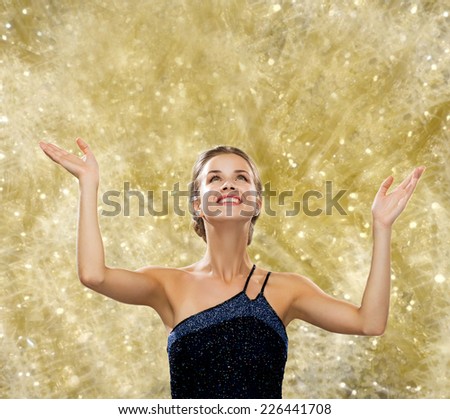 people, happiness, holidays and glamour concept - smiling woman raising hands and looking up over yellow lights background