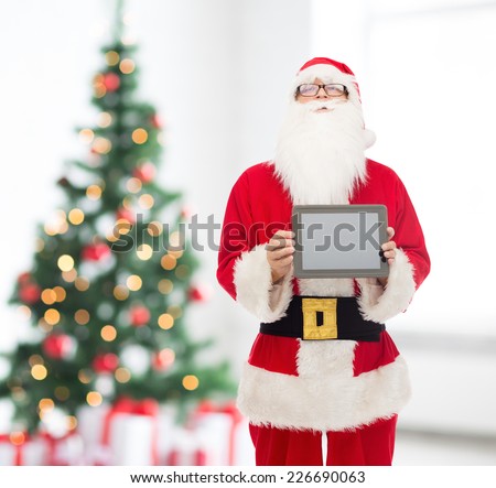 christmas, holidays, advertisement, technology and people concept - man in costume of santa claus with tablet pc computer showing blank screen over living room with tree background