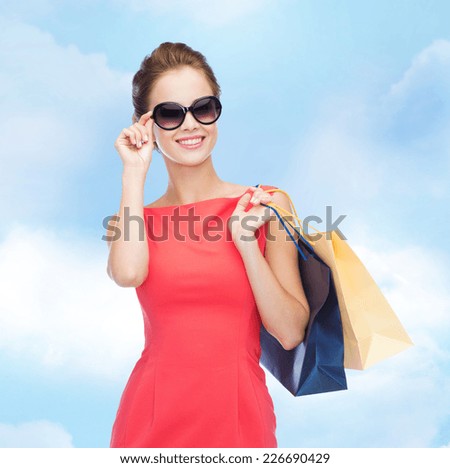 shopping, sale, christmas and holiday concept - smiling elegant woman in red dress and sunglasses with shopping bags