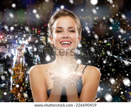 people, holidays, christmas and magic concept - laughing woman in evening dress holding something over snowy night city background