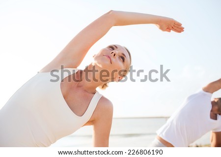 fitness, sport, friendship and lifestyle concept - close up of woman and man making yoga exercises on beach