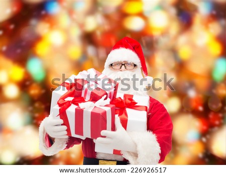 christmas, holidays and people concept - man in costume of santa claus with gift boxes over red lights background