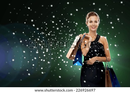 luxury, holydays, people and sale concept - smiling woman with shopping bags over snow and night lights background