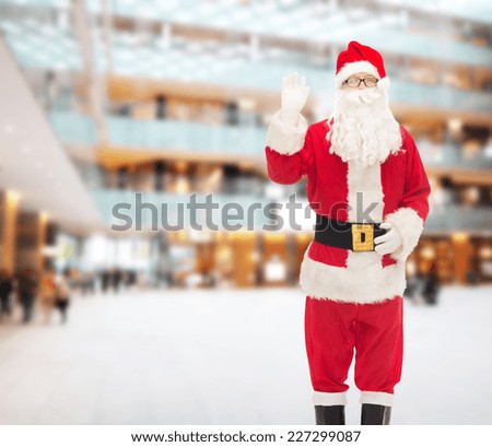 christmas, holidays, gesture and people concept - man in costume of santa claus waving hand over shopping center background