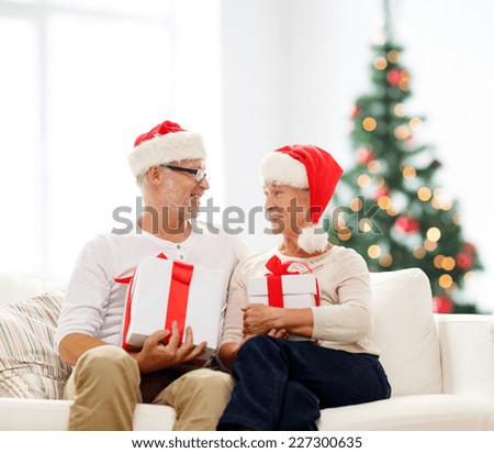 family, holidays, age and people concept - happy senior couple in santa helper hats with gift boxes over living room and christmas tree background