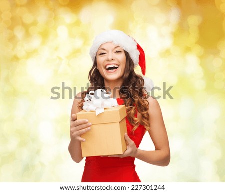 christmas, holidays, celebration and people concept - smiling woman in santa helper hat with gift box over yellow lights background