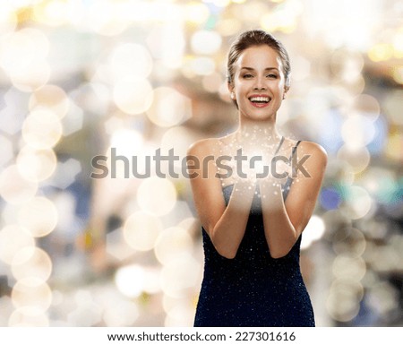 holidays and people concept - laughing woman in evening dress holding something over lights background