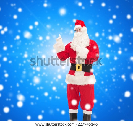 christmas, holidays, gesture and people concept - man in costume of santa claus pointing fingers over blue snowy background