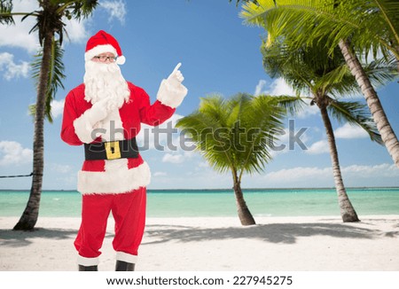 christmas, holidays, gesture and people concept - man in costume of santa claus pointing fingers over tropical beach background