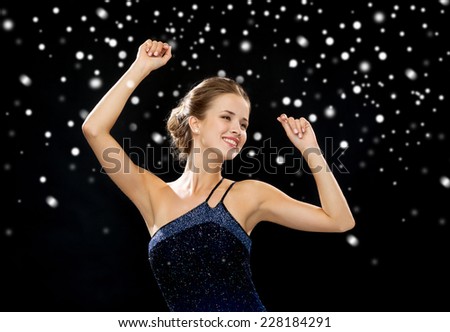 people, party, holidays, christmas and glamour concept - smiling woman dancing with raised hands over black snowy background
