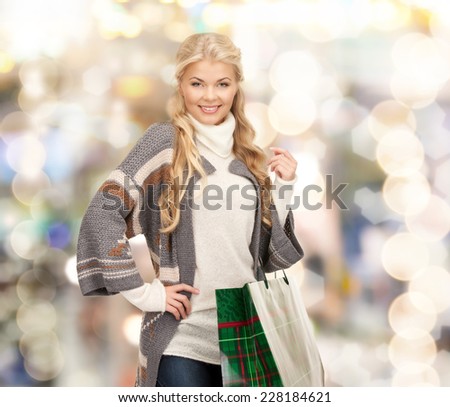 happiness, winter holidays, christmas and people concept - smiling young woman in winter clothes with shopping bags over lights background