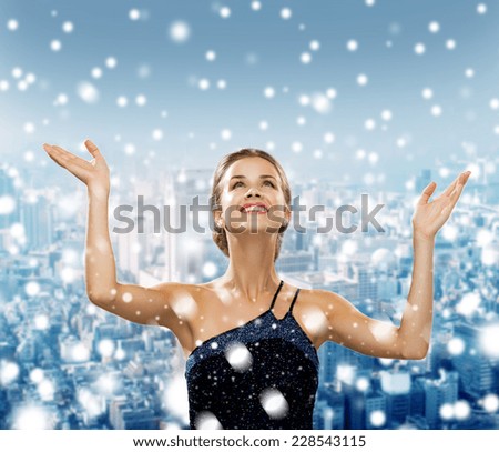 people, happiness, holidays and christmas concept - smiling woman raising hands and looking up over snowy city background