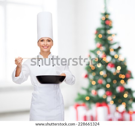 cooking, holidays, people and food concept - smiling female chef with pan and spoon tasting food over living room and christmas tree background