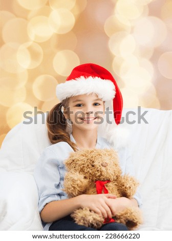 holidays, presents, christmas, childhood and people concept - smiling little girl with teddy bear toy over beige lights background