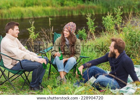 adventure, travel, tourism, friendship and people concept - group of smiling tourists drinking beer in camping